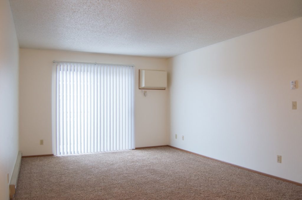 the living room of an apartment with a window and blinds. Fargo, ND Candlelight Apartments